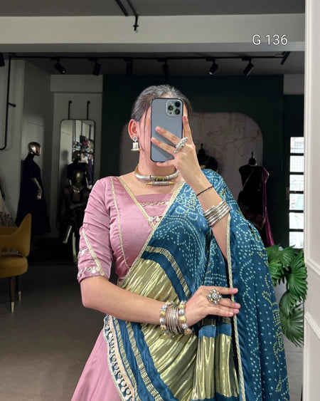 Woman taking a mirror selfie wearing a blue and green saree with a pink blouse.