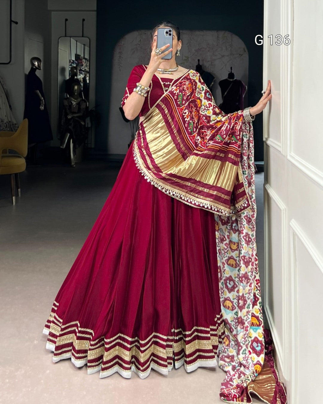 Woman wearing a traditional maroon saree with gold and floral patterns, standing indoors.
