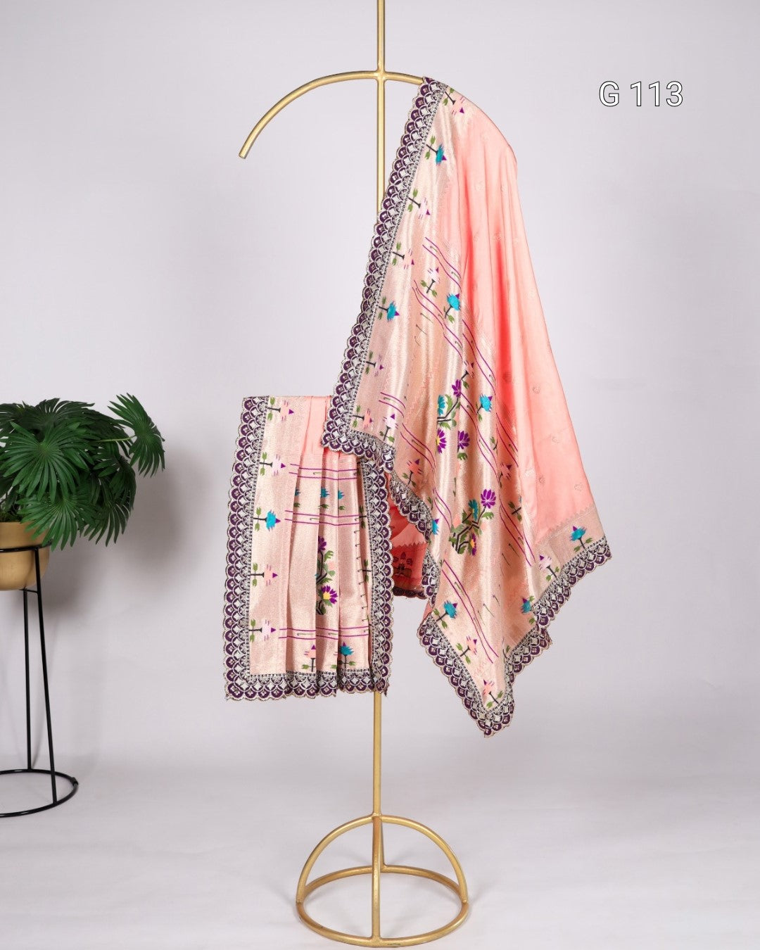 Pink saree with floral embroidery and decorative border on a gold stand against a white background