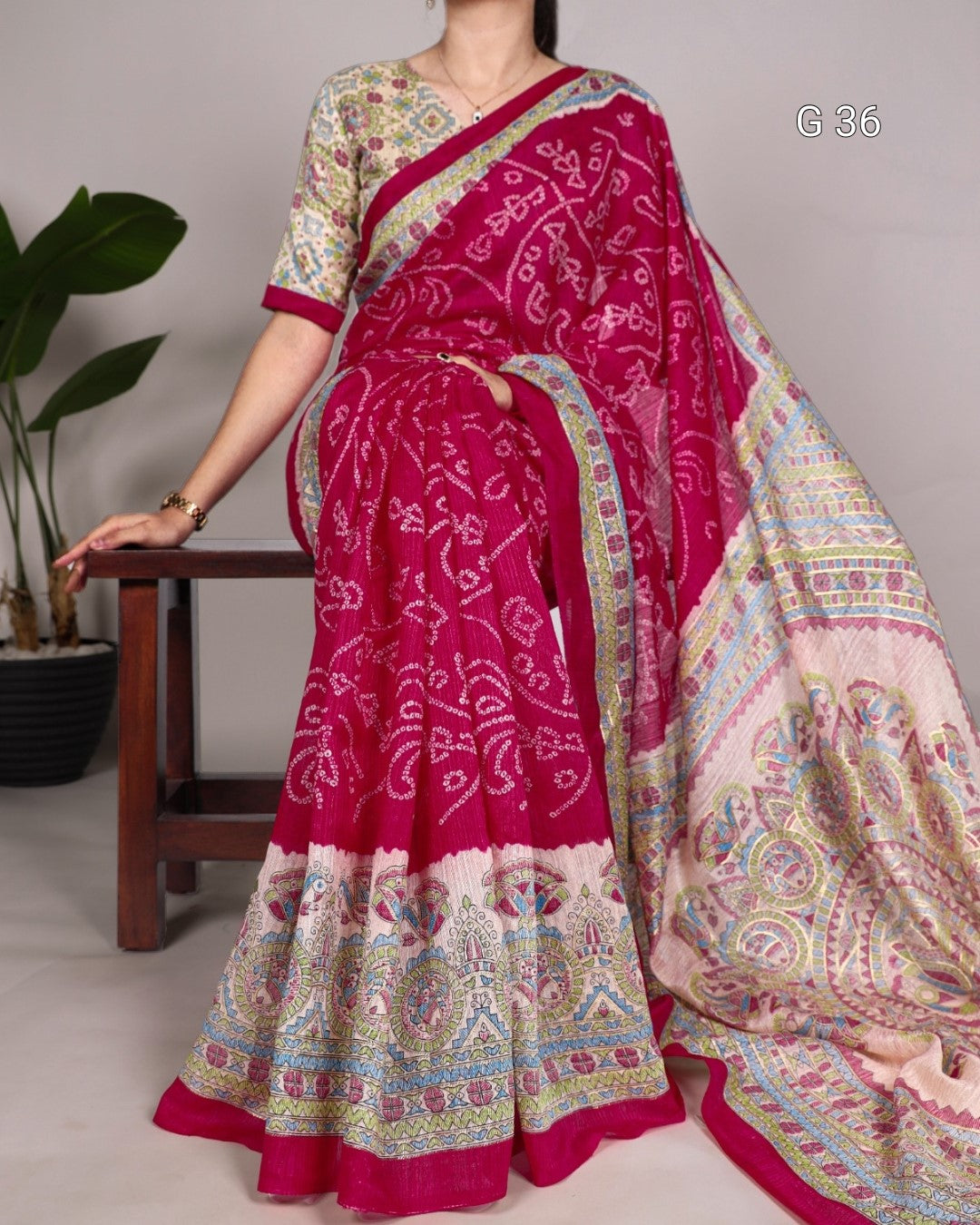 Woman wearing a pink saree with a patterned design, sitting on a chair.