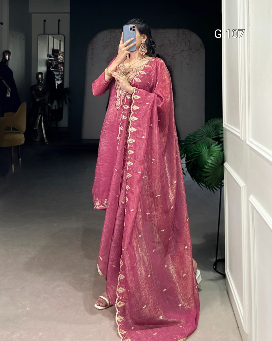 Person wearing a pink traditional outfit with gold embroidery in an indoor setting.