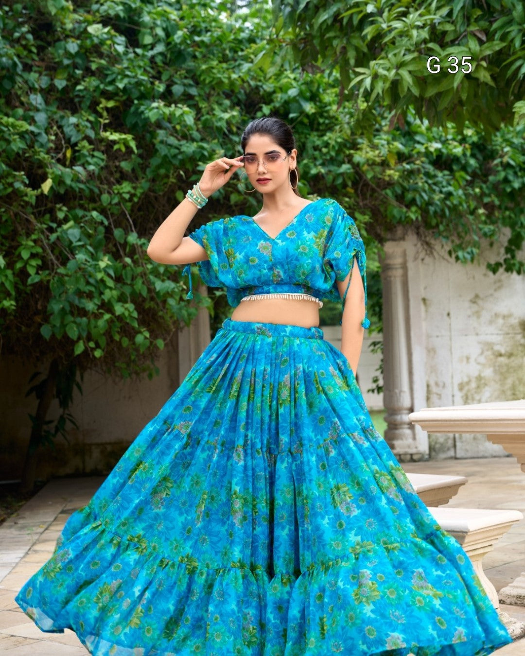 Woman wearing a blue floral traditional outfit standing outdoors with greenery in the background