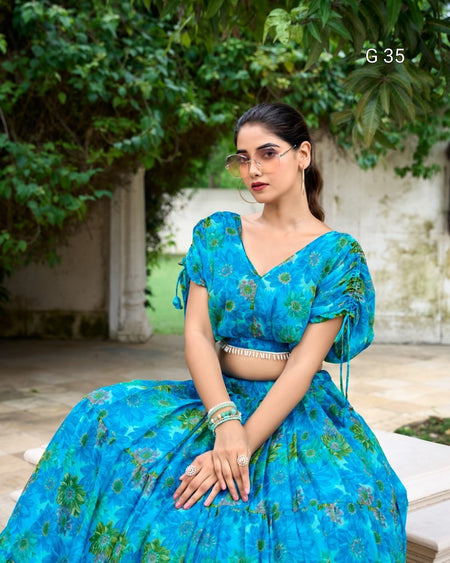 Woman wearing a blue floral outfit sitting outdoors with greenery in the background