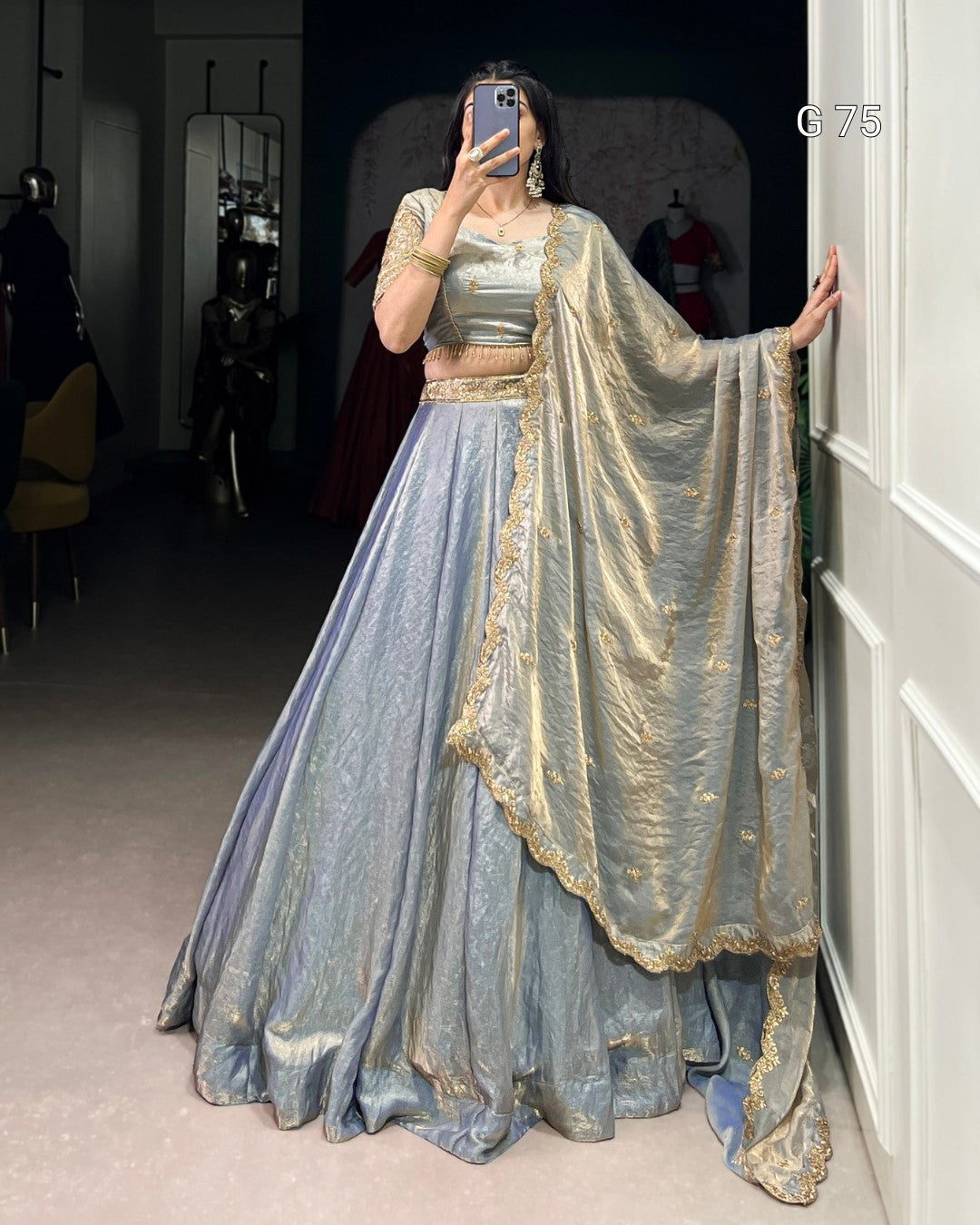 Person wearing a traditional outfit with a blue and gold dress and dupatta in a room.