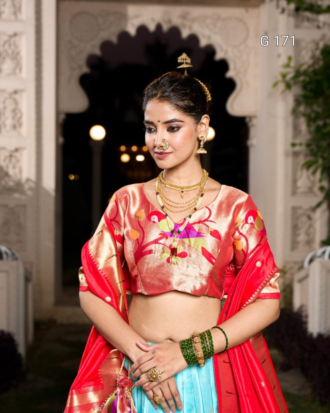 Woman in traditional Indian attire with jewelry, standing in an elegant setting.
