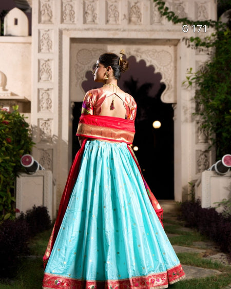 Woman in traditional outfit with red and blue colors standing in front of an architectural structure.