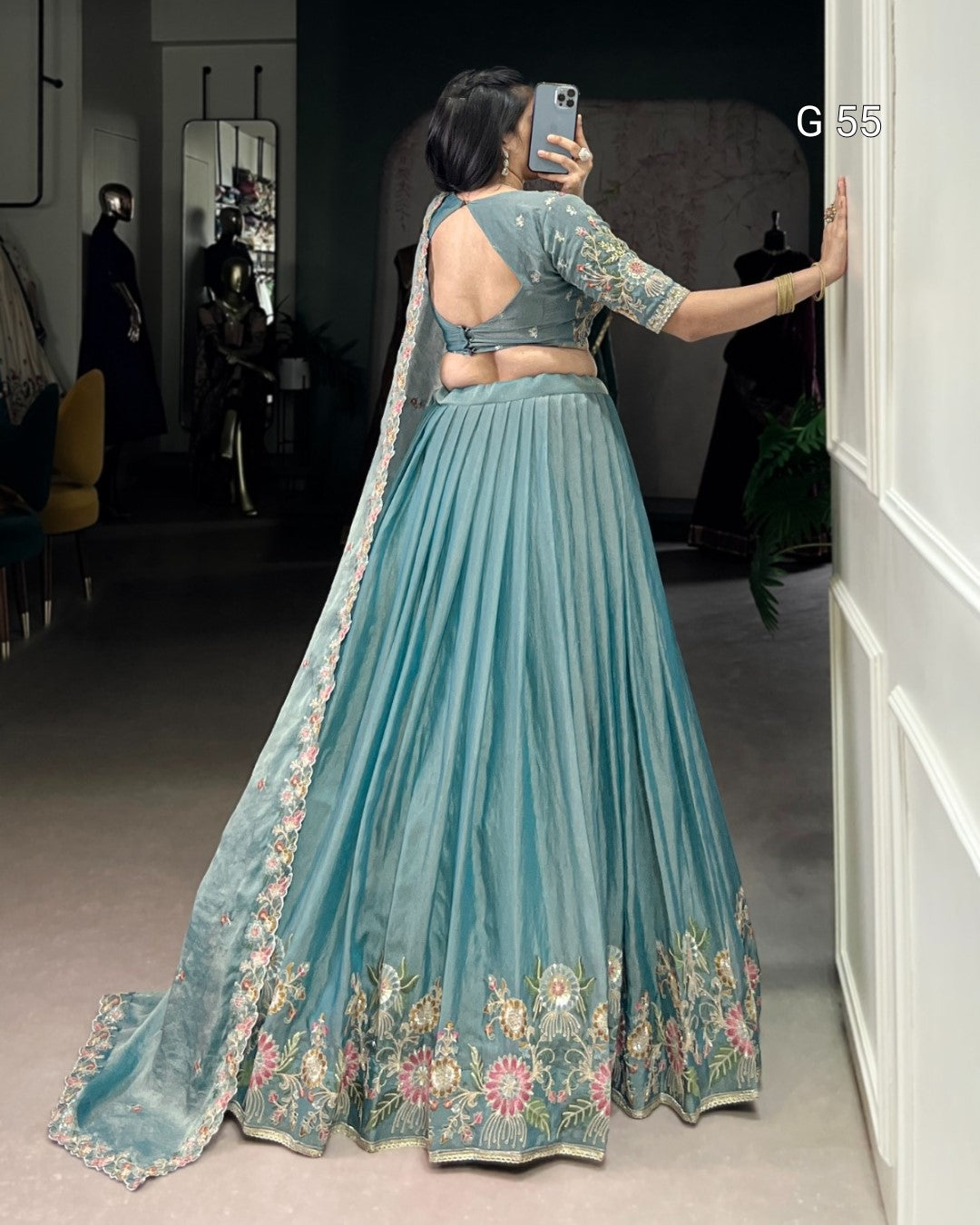 Woman in a teal embroidered lehenga taking a mirror selfie.