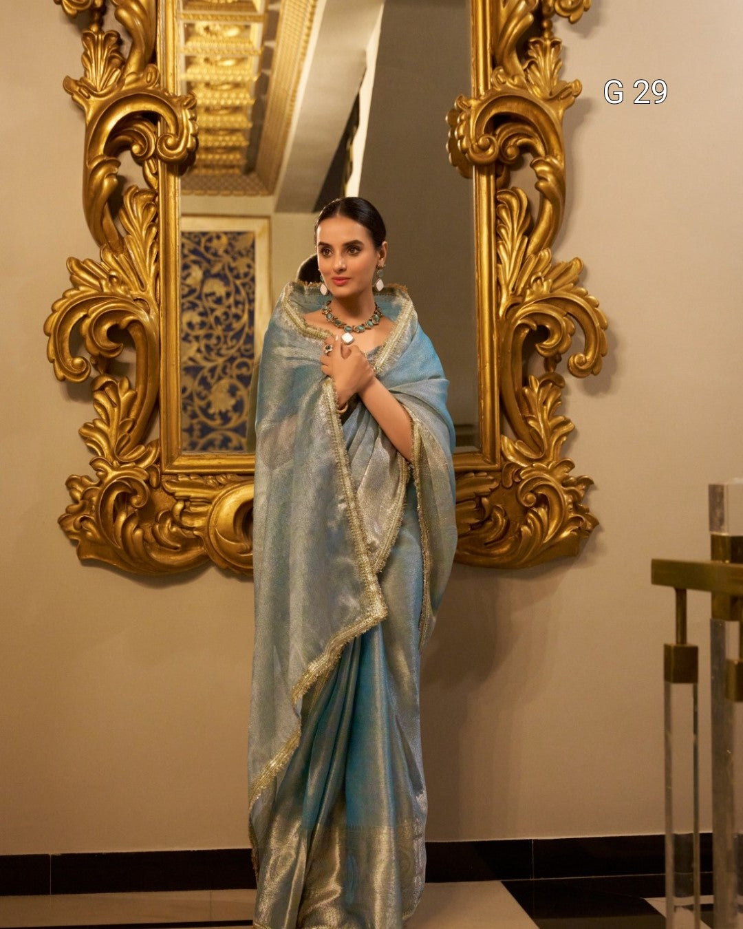 Woman in a light blue saree standing in front of an ornate gold mirror.