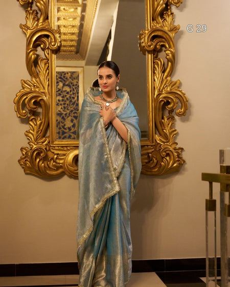 Woman in a light blue saree standing in front of an ornate gold mirror.