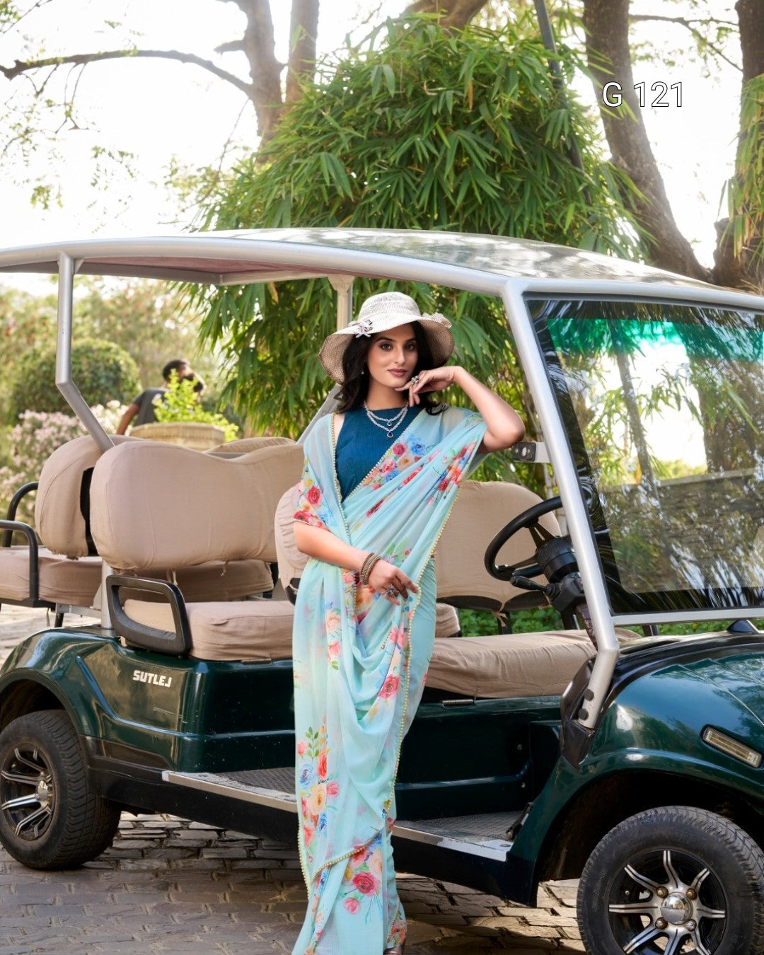 Woman in a floral saree standing next to a golf cart in a park-like setting