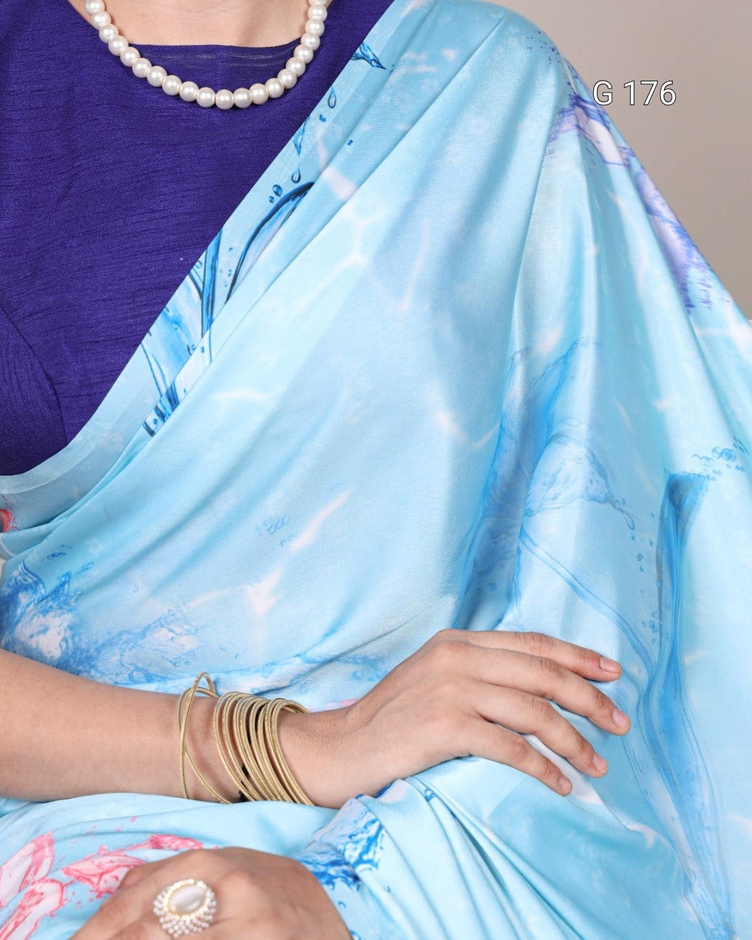 Person wearing a light blue saree with floral patterns, holding it with one hand.