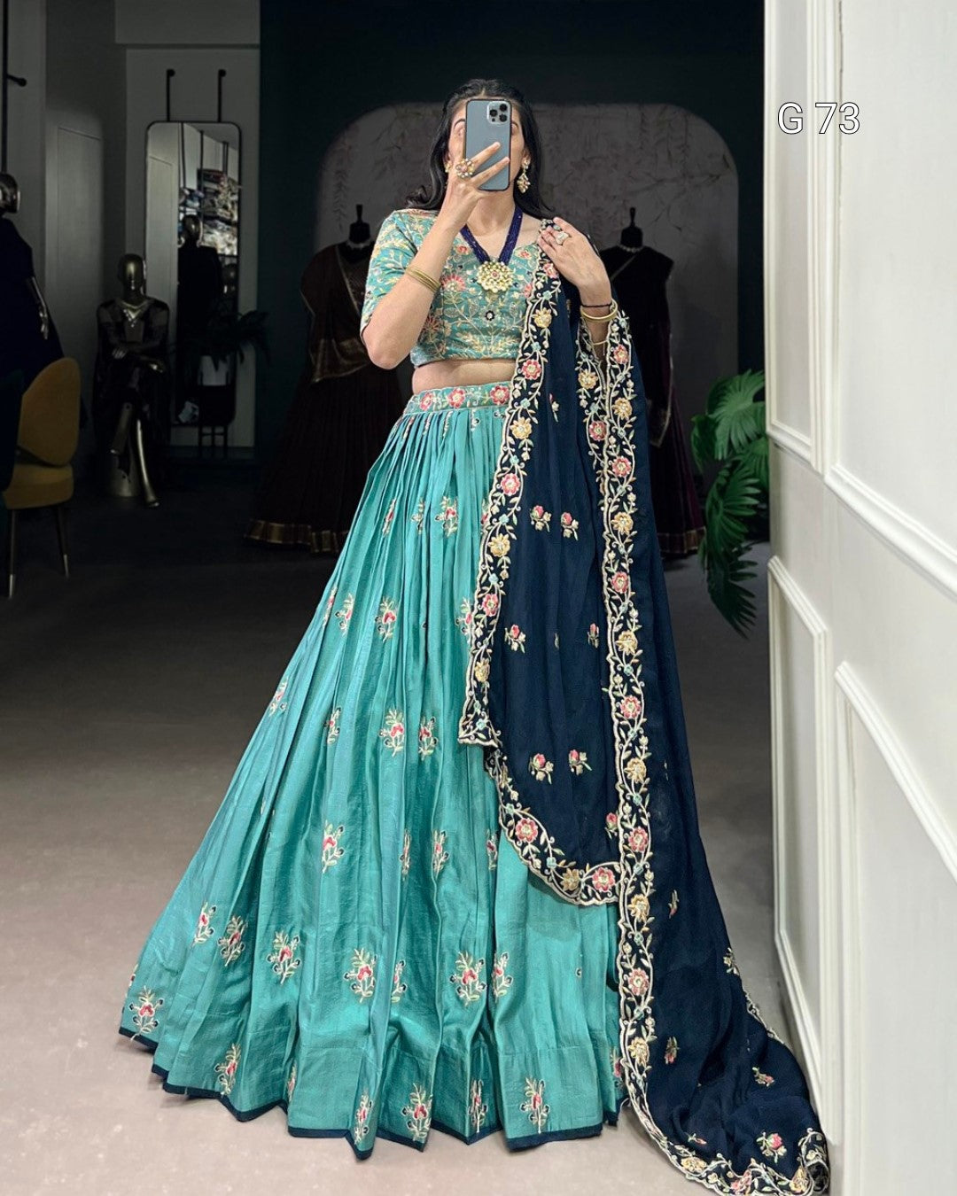 Person wearing a traditional outfit with a teal lehenga and navy dupatta in a room.