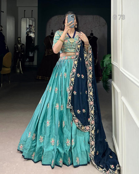 Person wearing a traditional outfit with a teal lehenga and navy dupatta in a room.