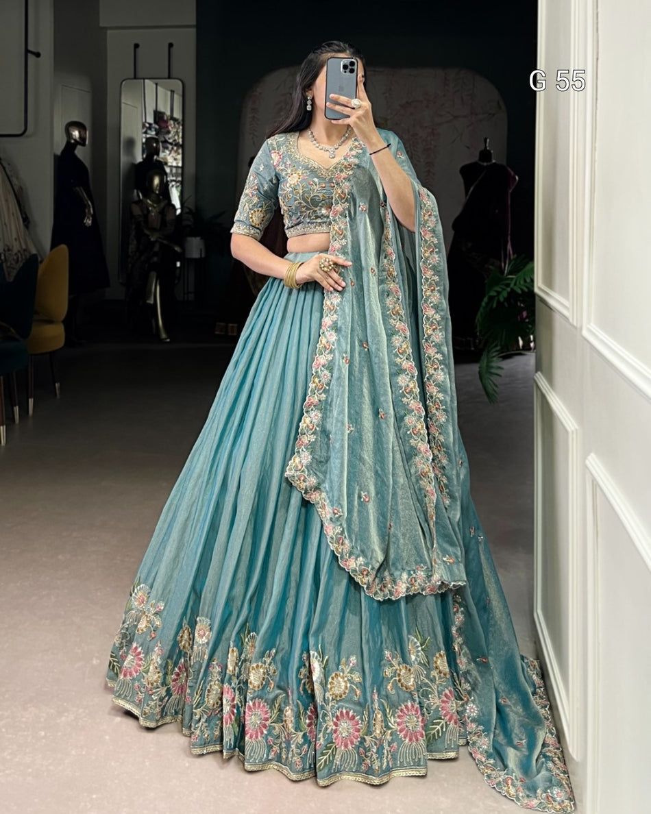 Person wearing a light blue embroidered traditional outfit in a room.