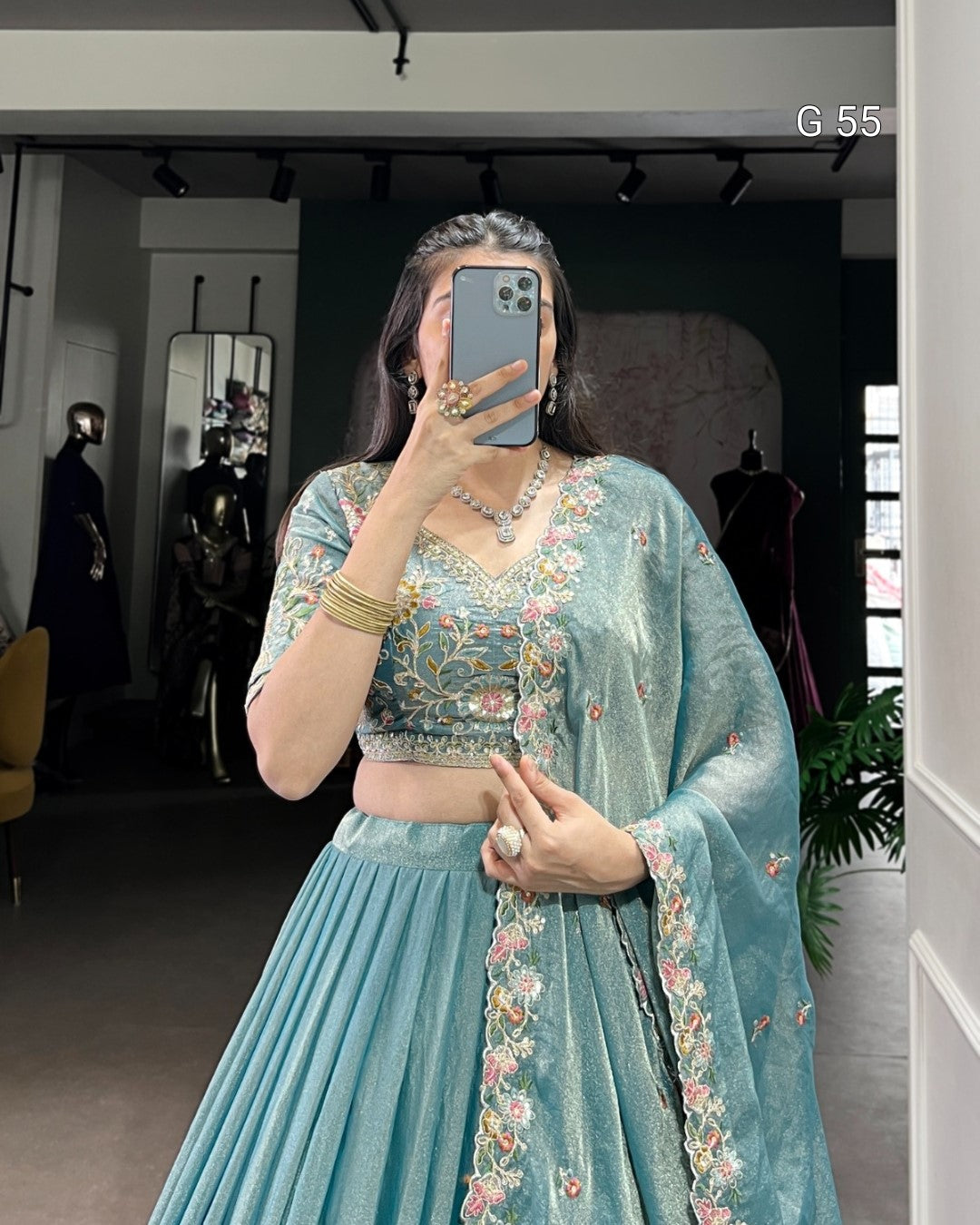 Person wearing a light blue embroidered traditional outfit in a room.
