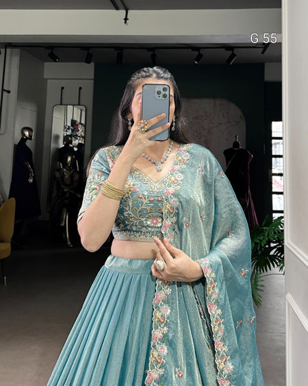 Person wearing a light blue embroidered traditional outfit in a room.