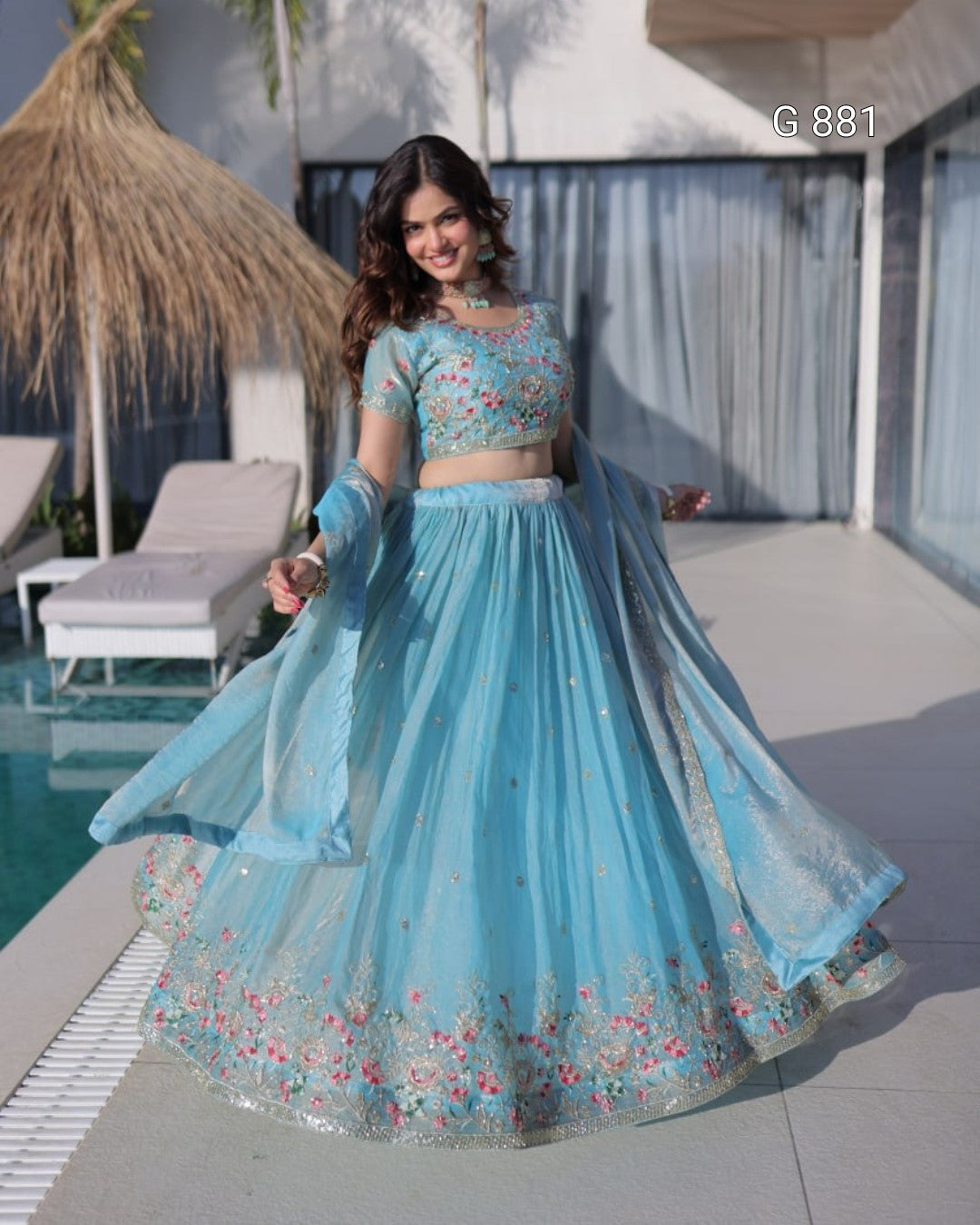 Woman in a light blue embroidered traditional outfit by a poolside.