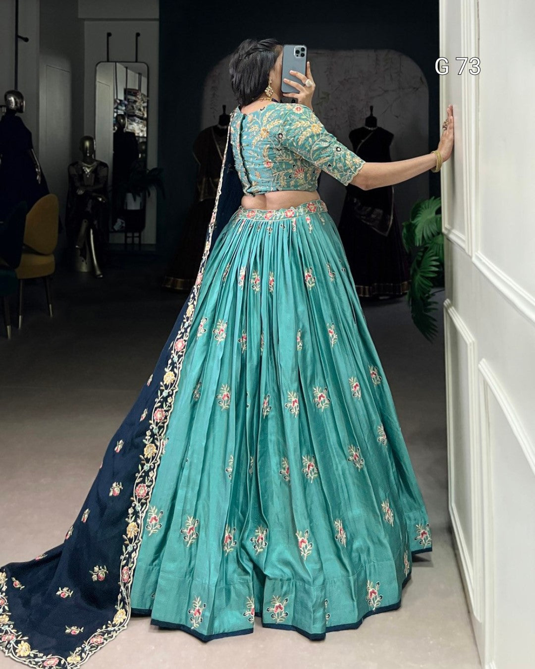 Person wearing a teal and navy embroidered traditional outfit taking a mirror selfie.