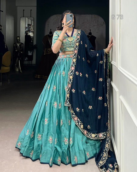 Person wearing a traditional outfit with a teal lehenga and navy dupatta, standing in a room.