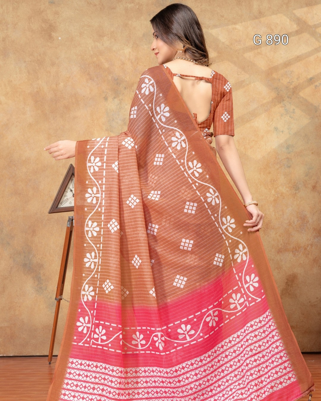 Woman wearing a brown and pink saree with white patterns against a beige background