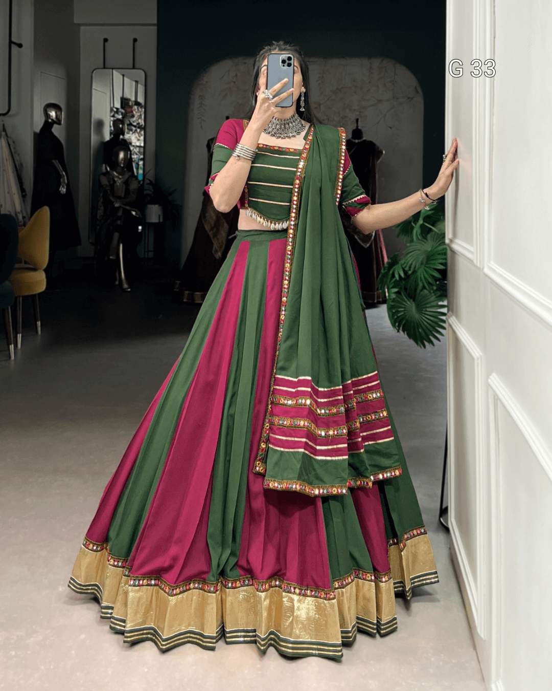 Person wearing a green and pink traditional outfit with gold accents, standing in a room.