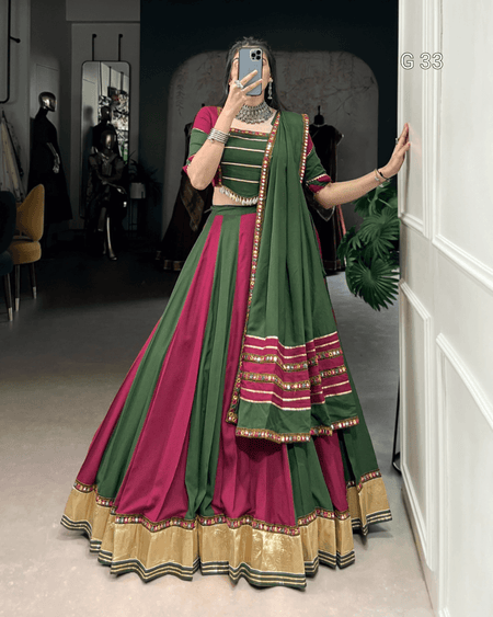 Person wearing a green and pink traditional outfit with gold accents, standing in a room.