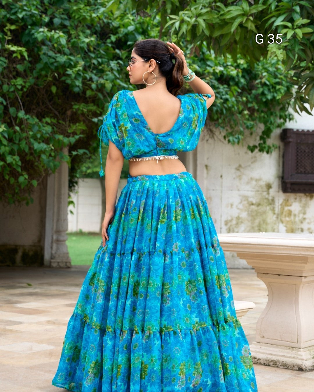 Woman wearing a blue floral dress standing outdoors with greenery in the background