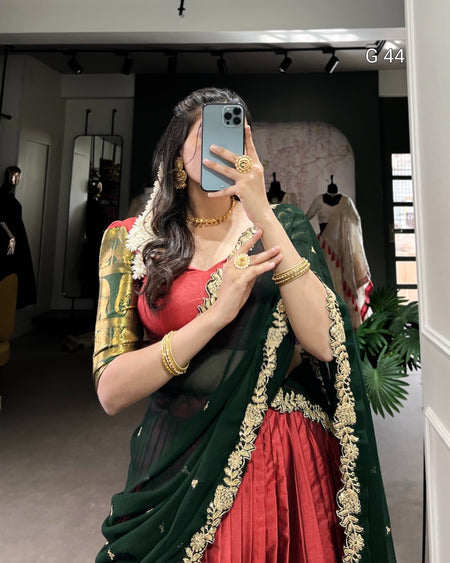 Woman taking a mirror selfie wearing a green and red saree with gold jewelry.