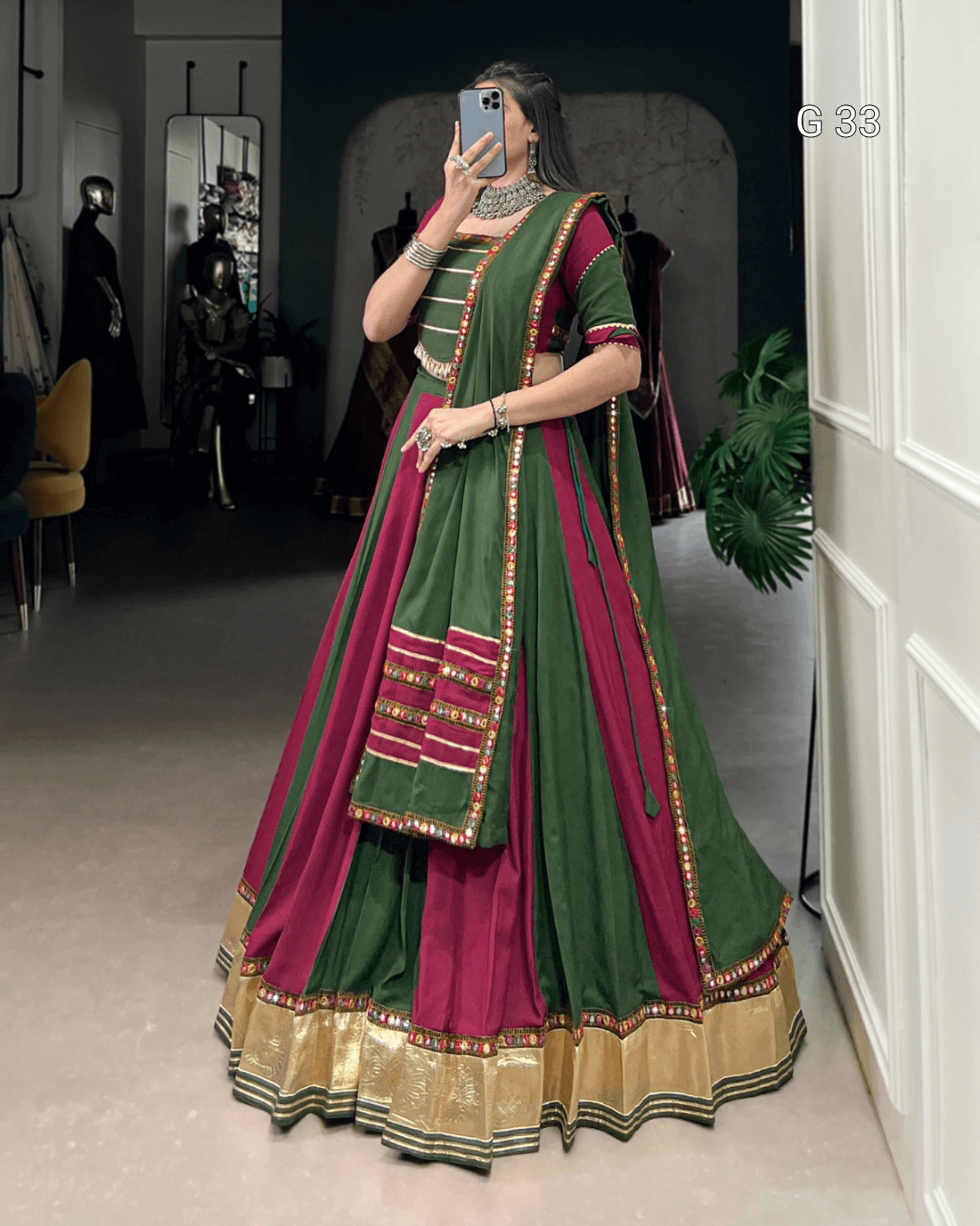 Person wearing a green and red traditional outfit with gold details, standing indoors.