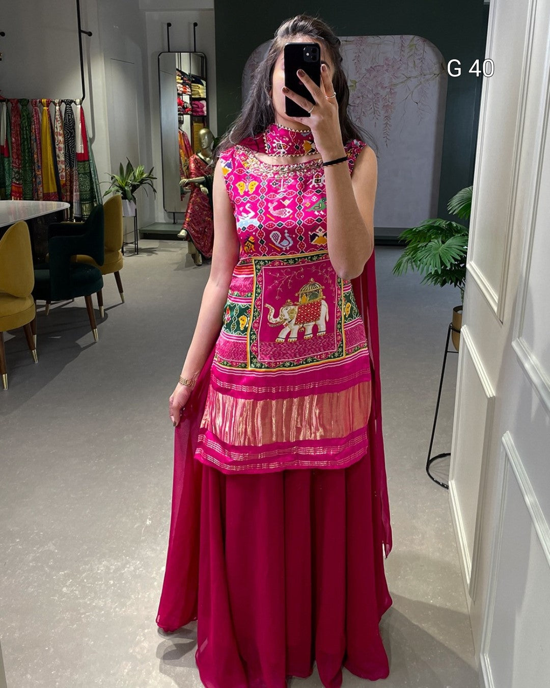Person wearing a vibrant pink traditional outfit with colorful patterns in a room.