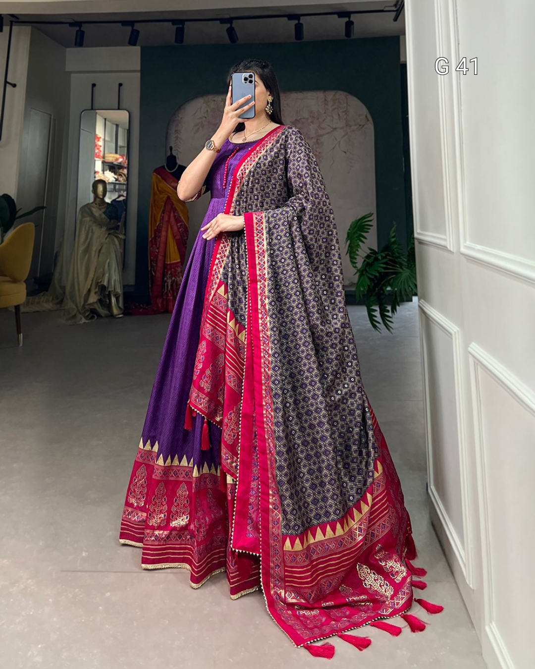 Person wearing a traditional outfit with a purple and pink dupatta in a room.