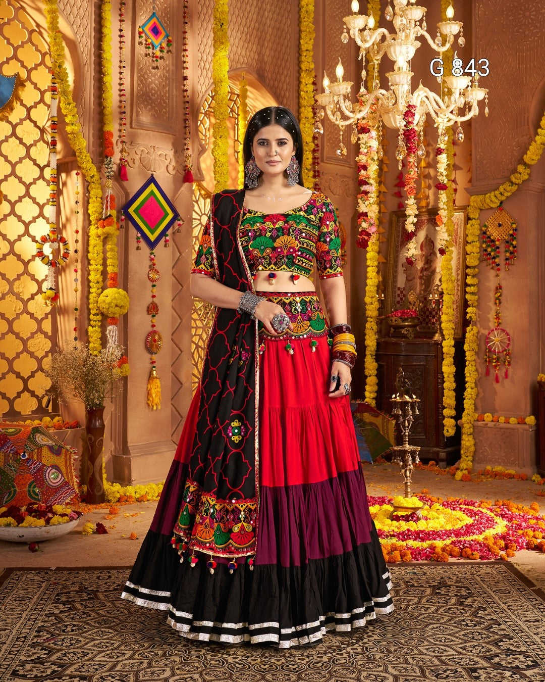 Woman in a traditional multicolored outfit with intricate patterns in a decorated indoor setting.