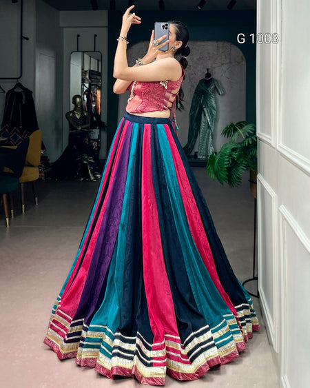A woman takes a mirror selfie in a boutique wearing a vibrant, multi-colored traditional Indian skirt set (lehenga) with pink, teal, and navy blue vertical stripes and a matching embroidered crop top.