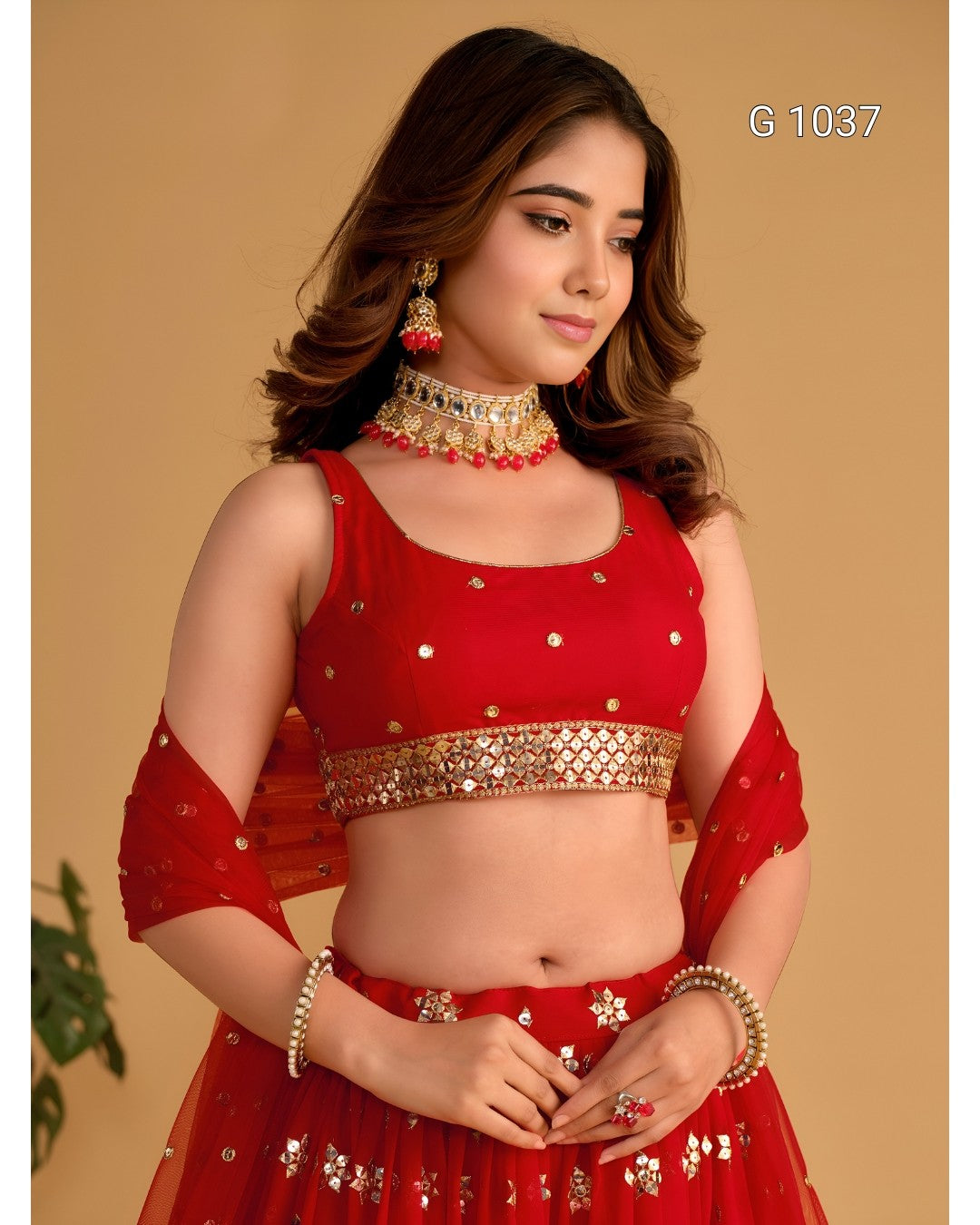 A woman modeling a red Indian ethnic outfit with gold embellishments, featuring a crop top, matching skirt, and ornate jewelry against a beige background. The text 'G 1037' is visible in the top right corner.