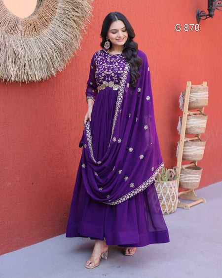 Woman wearing a purple traditional outfit with gold embroidery against a red wall.