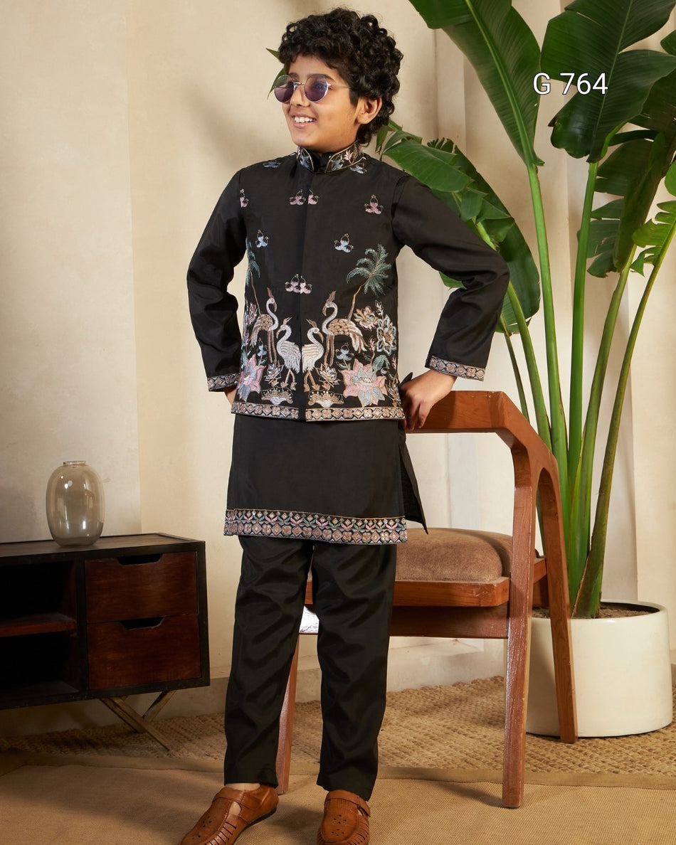 Young boy in a traditional outfit standing in a room with a plant and wooden chair.