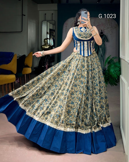 A woman takes a mirror selfie in a boutique wearing a traditional Indian anarkali gown. The dress features a blue and gold floral printed skirt with a solid royal blue pleated border, and a blue sleeveless bodice with gold embroidery.