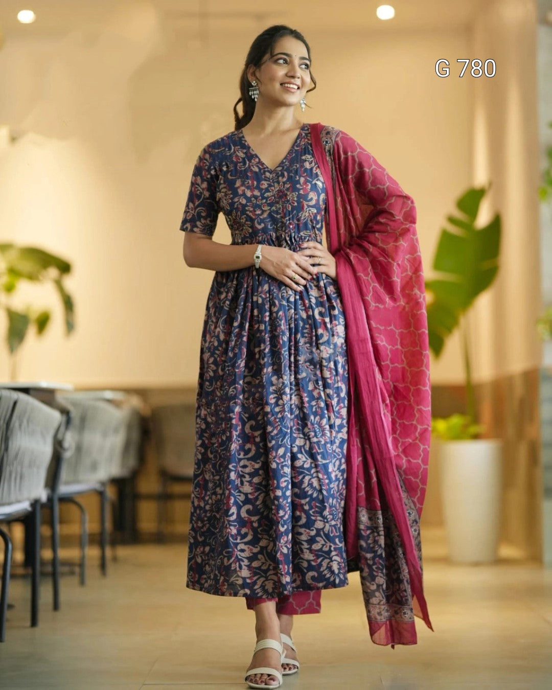 Woman in a blue floral dress with a pink dupatta standing indoors.