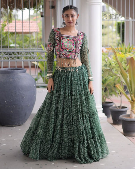 A woman modeling a dark green embroidered traditional Indian outfit with a heavily patterned embroidered bodice and a matching flared skirt, standing in a porch setting with potted plants.