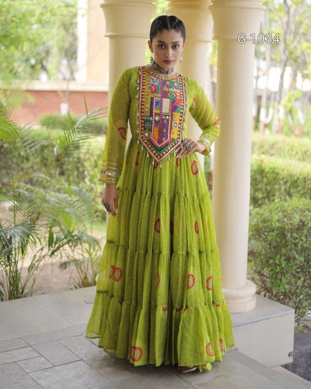 A woman models a vibrant lime green Anarkali gown with a heavily embroidered multicolor yoke and tiered skirt, standing in front of cream-colored pillars and green garden foliage.