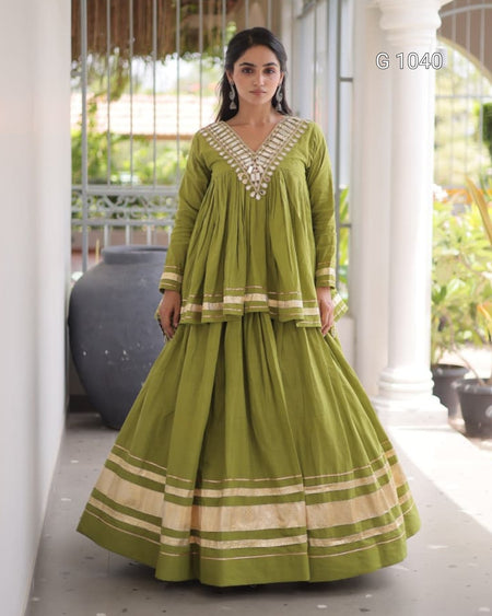 A woman models a green traditional Indian outfit with beige stripes and silver embroidery on a porch with white pillars.