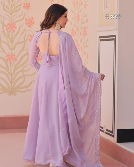 Woman in a lavender saree with a floral wall and door in the background