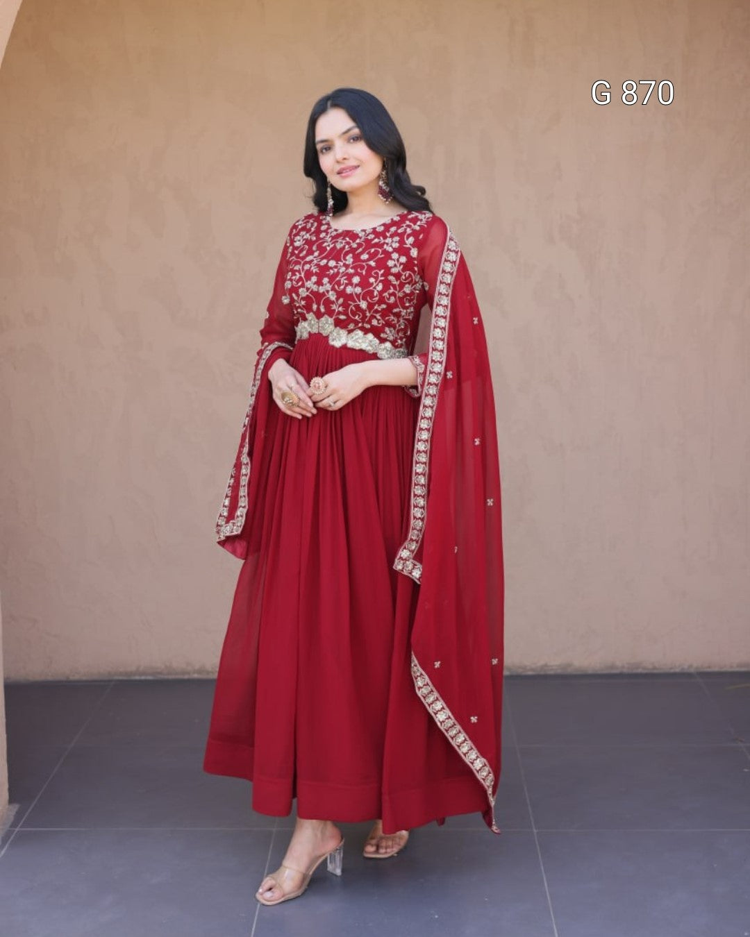 Woman wearing a red traditional outfit with a matching dupatta against a plain background
