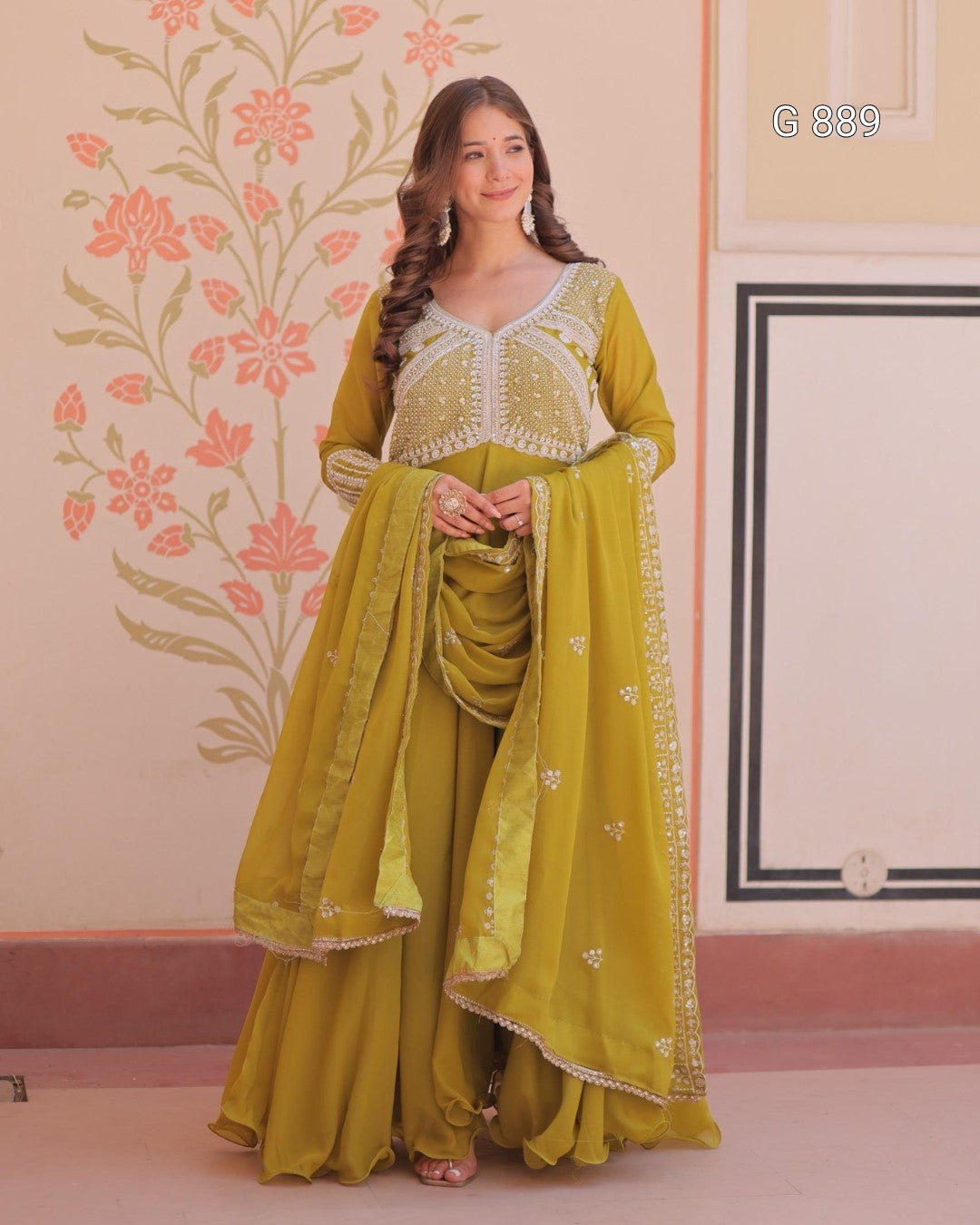 Woman in a green traditional outfit with floral patterns on a decorated wall.