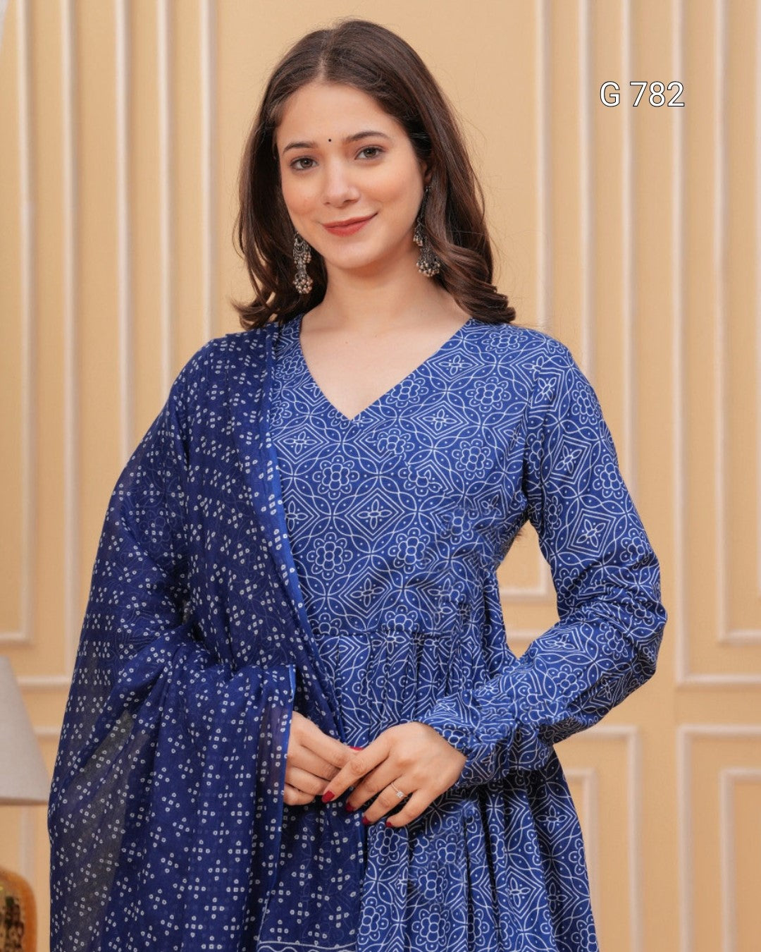 Woman wearing a blue patterned dress against a beige wall.