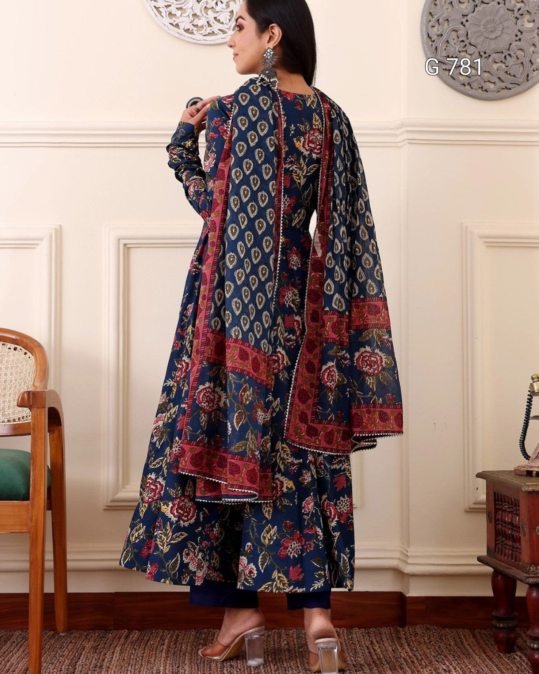 Woman wearing a floral patterned outfit in a room with white walls and wooden furniture.