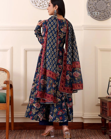 Woman wearing a floral patterned outfit in a room with white walls and wooden furniture.