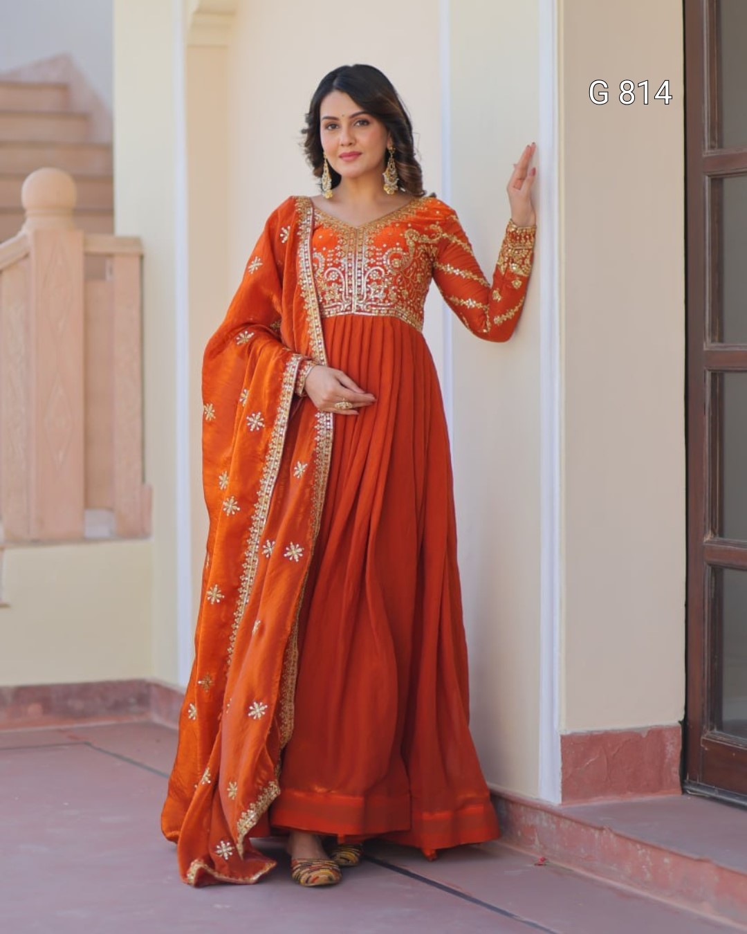 Woman wearing an orange traditional outfit with gold embroidery indoors.