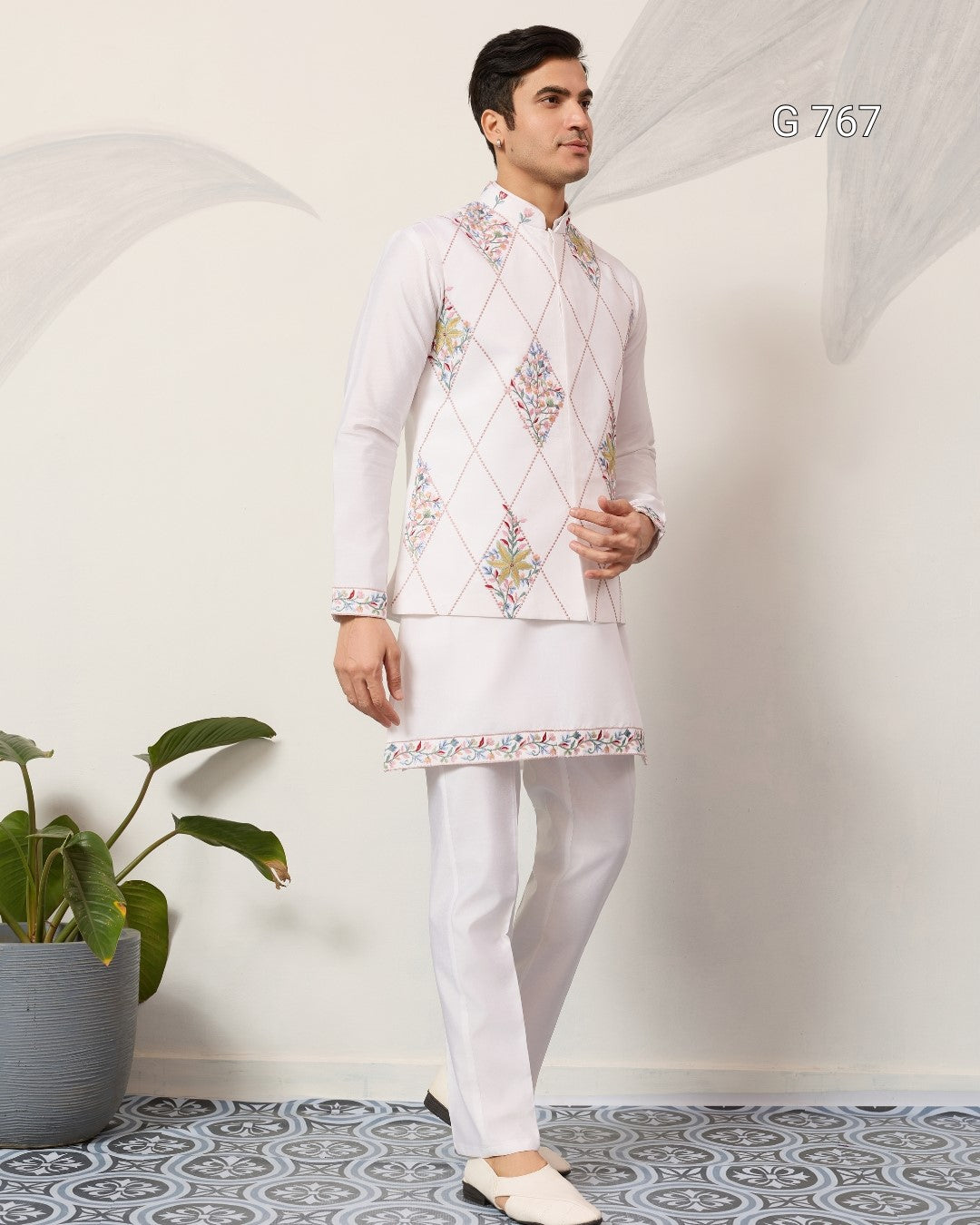 Man wearing a traditional white embroidered outfit with a plant in the background