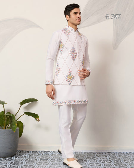 Man wearing a traditional white embroidered outfit with a plant in the background